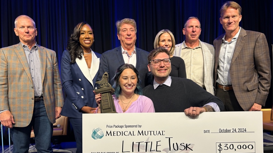 Lauran and Jordan Woolley display one of the cash prize awards their company, Little Tusk, won at Thursday’s Shark Tank competition. Behind them are judges, from left, Don Thomas, managing partner of Platz Realty;Ashley Vidale, co-owner of Sapphire Aesthetics and Wellness; Sam Boak, president of Boak & Sons Inc.; Stacy Howlett, CEO of Howlett Logistics; Bo Pelini, investor and former head football coach at the University of Nebraska and Youngstown State University; and Rob Cochran, chairman of #1 Cochran.